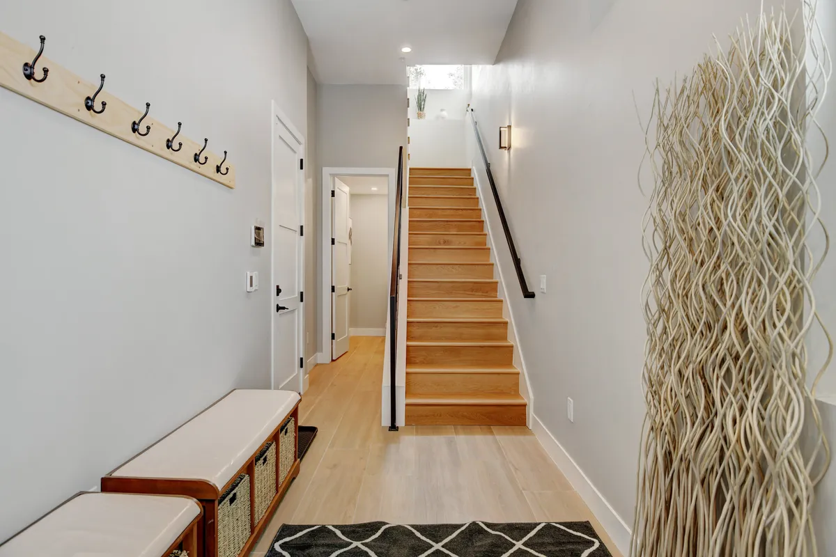 A welcoming mudroom featuring a coatrack, bench with storage, a decorative plant, and a staircase. The space is designed for practicality, allowing easy organization and transition in and out of the home, perfect for handling boots, coats, and outdoor gear.