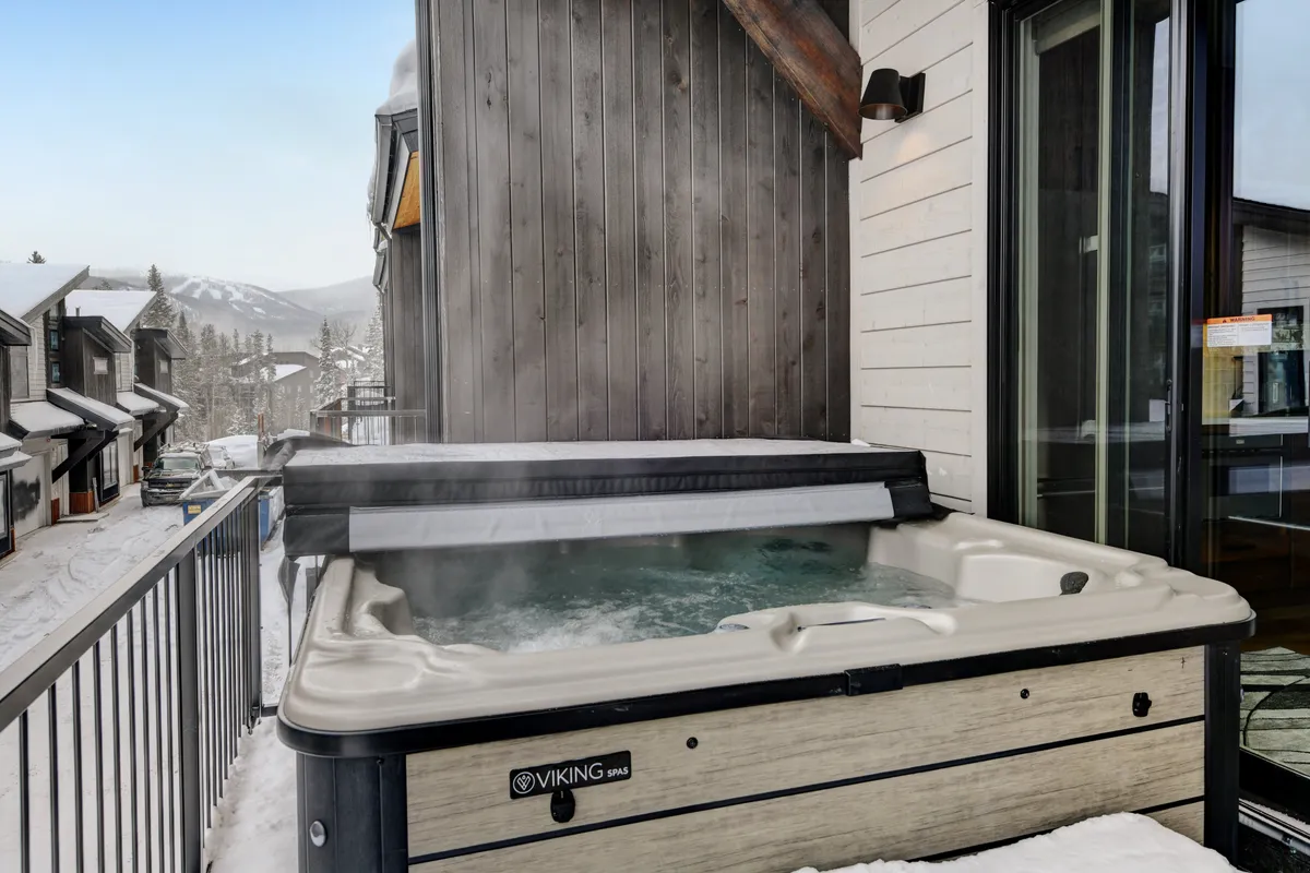 This striking exterior image centers on a private hot tub set against a snow-covered landscape, with breathtaking mountain views stretching into the distance. The setting is both secluded and luxurious, emphasizing relaxation while immersed in the dramatic scenery of the Rockies. The warm bubbling water contrasts beautifully with the winter backdrop, suggesting cozy comfort even amid the elements.