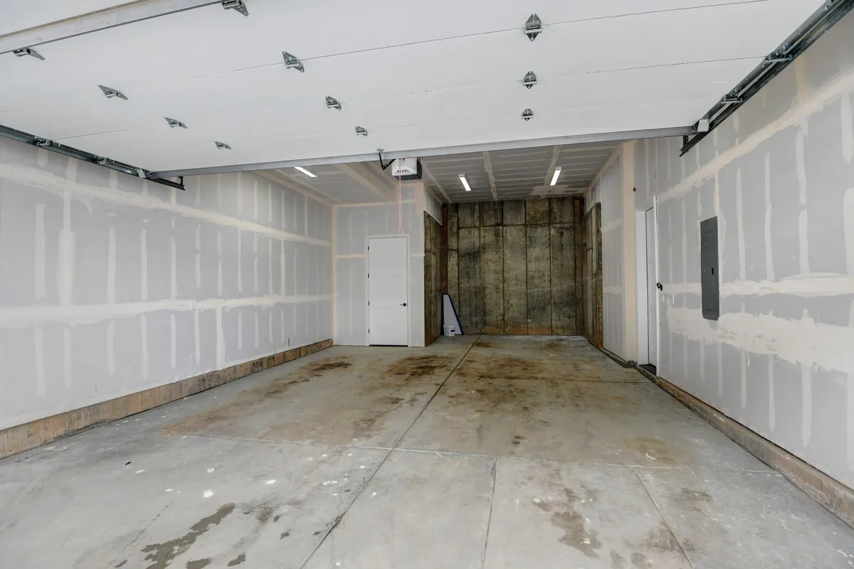 A spacious, empty garage with a concrete floor and drywall surfaces, offering ample room for storing vehicles, bikes, skis, and other adventure gear. The utilitarian design provides flexibility for customizing the space for various storage needs.