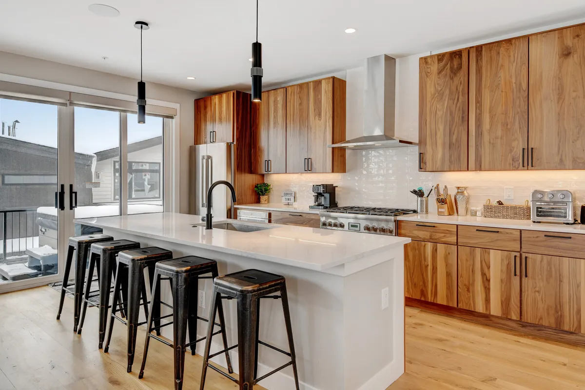 A contemporary kitchen scene with a kitchen island, bar stools lined up for breakfast or snacks, and a window offering natural light. The setting is designed for both cooking and casual dining, with an open, welcoming layout.
