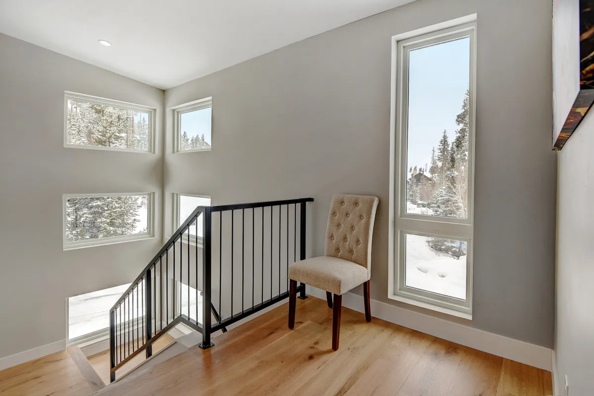 A serene scene with a staircase, a comfortable chair perfectly positioned by large windows, and a panoramic view outside. The space is filled with natural light, evoking a sense of quiet reflection and connection to the outdoors.