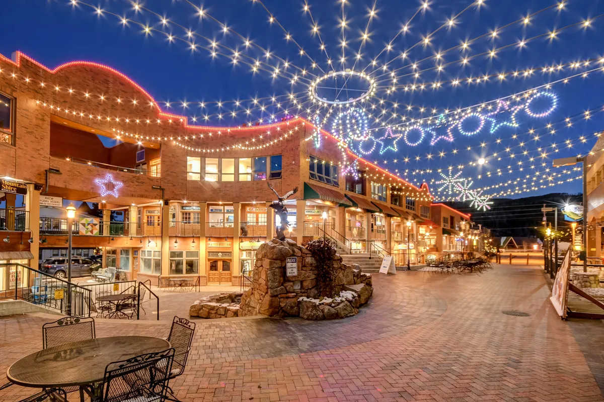 A lively exterior scene with string lights, star decorations, a stone fountain, and plenty of inviting outdoor seating, evoking the feel of a town square ready for social gatherings, holiday markets, or casual strolls.