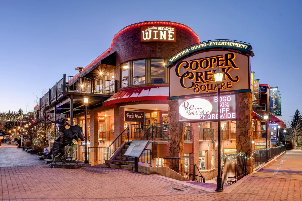 A vibrant exterior shot of Cooper Creek Square, featuring a wine shop, decorative lighting, and inviting public spaces. The festive mood signals a lively local scene, with opportunities for shopping, dining, and socializing just moments away.
